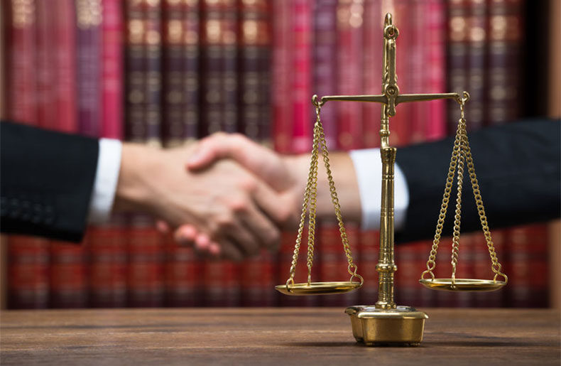 Handshake representing a client hire a lawyer next to scales of justice in front of red books